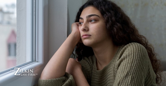 Teenage girl looking outside a window with her head leaning against her hand.
